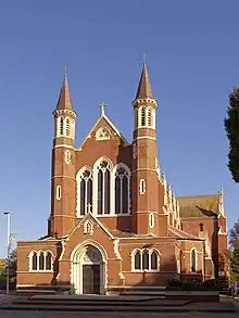 A front facing view of Portsmouth's Roman Catholic cathedral, St John the Evangelist. The cathedral itself is made of brick and has a large chancel and nave at the front. Stained windows are also seen above the front door.