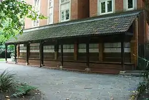 A long dark wooden structure. On the wall of the wooden structure, parallel rows of pale tiles are visible.