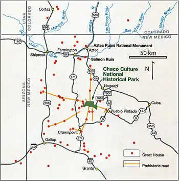 Large square map of northwestern New Mexico and neighboring parts of, clockwise from left, western Arizona, southeastern Utah, and southwestern Colorado. The map region has a green and blocky rectangular-crescent area at its center labeled Chaco Culture National Historical Park. Radiating from the green region are seven segmented gold lines: "[p]rehistoric roads", each several dozen kilometers in length when measured according to the map scale factor. Roughly seventy red dots mark the location of great house[s]; they are widely spread across the map, many of them far from the green area, near the extremes of the map, more than one hundred kilometers from the green area. Two proceed roughly south, one southwest, one northwest, one straight north, and the last to the southeast. Yellow dots mark the location of modern settlements: Shiprock, Cortez, Farmington, and Aztec to the northwest and north; Nageezi, Cuba, and Pueblo Pintado to the northeast and east; Grants, Crownpoint, and Gallup to the south and southwest. They are connected by a network of gray lines marking various interstate and state highways. A fan of thin blue lines along the northern margins of the map depict the San Juan River and its communicants.