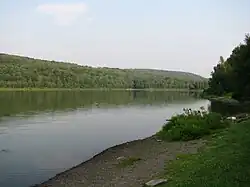 A lake with a gravel shore in the foreground and a forested distant shore