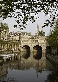 Water in the foreground reflecting an arched bridge of honey-coloured stone.