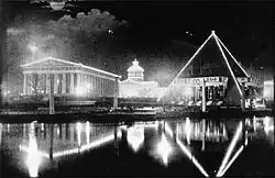 A black and white photo showing a lit Parthenon and pyramid