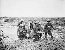 Several British soldiers, knee deep in mud, carry a wounded comrade on a stretcher.