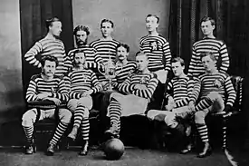 A group of footballers wearing black and white hooped jerseys posing with a football and trophy