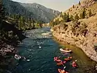 River rapids cut through a mountain landscape, with several boaters visible in the foreground