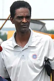 A man, wearing white shirt with a logo and the word "NBA PLAYERS" on the front, is standing and posing for a photo.