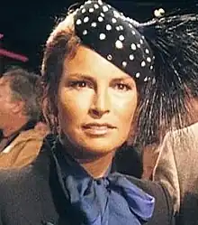 Welch in a blue scarf and high-collared gray jacket, with polka-dot feathered cap