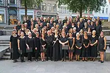 2016 photograph of a choir on stairs outside the Bruges Cathedral, with the Old Town in the background