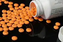 A pill bottle on its side with orange circular tablets spilled out