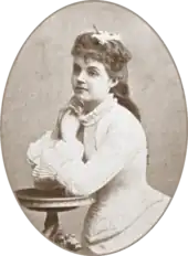 teenage white woman in 19th-century costume seated, with both elbows on a side table and her hands to her face