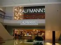 A two-story shopping mall concourse leading to a department store. Present are two signs reading "Kaufmann's"