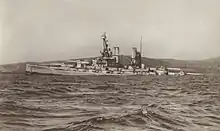 A large light grey battleship tilts back in choppy water as it slowly sinks.