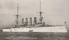 A large white warship at anchor in a calm sea, with a small boat alongside