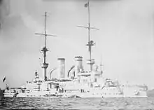 A large warship moored offshore, with several small boats alongside