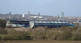 Football stadium with fields and trees in the foreground and town of Kirkcaldy in the background.