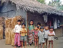 Group of smiling children in front of a thatch-roofed house