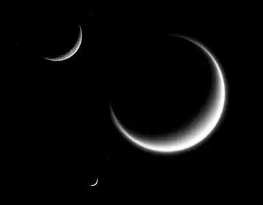 Titan (largest) together with Rhea and Mimas (smallest) in crescent shape, forming a triple crescent. Titan's massive atmosphere is clearly seen extending out into space, while Rhea and Mimas have none.