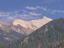 A light brown, almost white mountain rises above forested hills