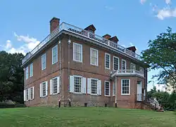 A two-story brick house with white wooden window trim and shutters seen from its corner