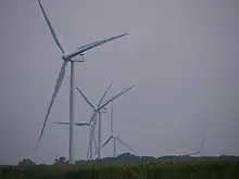 Five turbines of the Scioto Ridge Wind Farm in a zoomed narrow-angle shot, some of which are partially below the horizon due to distance and topography.