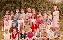 Group of seated children at a standing woman