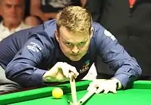 Shaun Murphy leaning over a table lining up a shot using a bridge stick