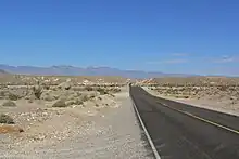 A two-lane asphalt highway passes through a desert landscape dotted with sagebrush and cacti as it heads towards the distant mountains in 2006.