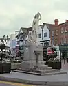 Statue on a plinth of a woman in classical dress carrying a jug on her shoulder and holding a child's hand. Steps up to the base of the plinth lead to a drinking fountain.