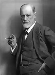 photograph of a balding man with a beard; holding a cigar and wearing a suit