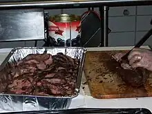 A member of the catering staff slices the pre-cooked beef loin into slices behind the scenes at a beefsteak