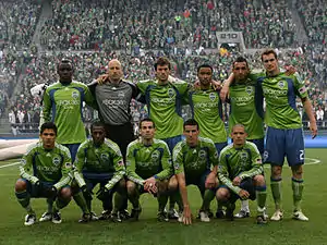 11 soccer players standing in 2 rows on a green field