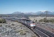 Two locomotives leading several railcars through the desert