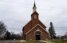 dark red brick church with a tall steeple. St. Edward's cemetery is visible in the far background