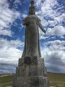 A large stone statue, atop a podium, of a robed woman with an elaborate headdress.