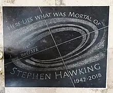 A black stone slab with a grey spiral, an equation, and the words "Here lies what was mortal of Stephen Hawking 1942–2018".