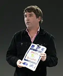 Stephen Hillenburg stands holding a book looking off to his right