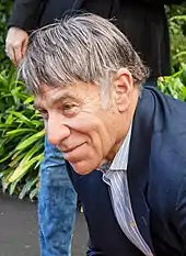 A man wearing a black blazer and shirt signing autographs onto a newspaper