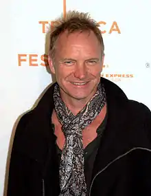 A Caucasian male wearing all black and a floral scarf around his neck.