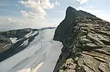 Mountain range composed of dark rock with traces of snow on the sides, against a cloudy blue sky.