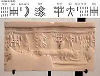 Impression of an Indus cylinder seal discovered in Susa, in strata dated to 2400–2100 BC. Elongated buffalo with line of standard Indus script signs. Tell of the Susa acropolis. Louvre Museum, reference Sb 2425. Indus script numbering convention per Asko Parpola.