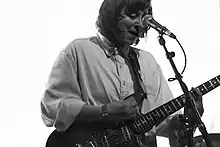 Person playing guitar with microphone in front of them, and an all-white background.