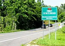 View of a two-lane road with a large green sign in the background