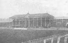 View towards one end of the ground, showing a roof, supported by several pillars and bearing a clock, covering the central part (behind the goal) of an otherwise open terrace