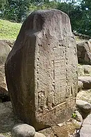 An upright stone slab with the front face flat and inscribed with two elaborately dressed figures facing each other, with a double column of hieroglyphs between them.