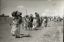 Women carrying bags while walking with men and children