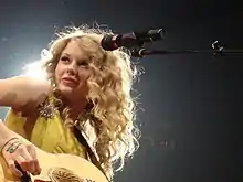 Swift playing a guitar, donning a yellow dress