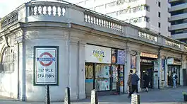 A grey building with a rectangular, white sign on a rounded corner reading "TEMPLE STATION" in black letters all under a blue sky