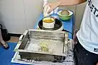 Person pouring a viscous yellow liquid into water