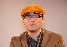 A bespectacled Tensai Okamura, wearing an orange cap