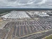 Gigafactory Berlin-Brandenburg in Grünheide, on the edge of a highway with an industrial park in the distance